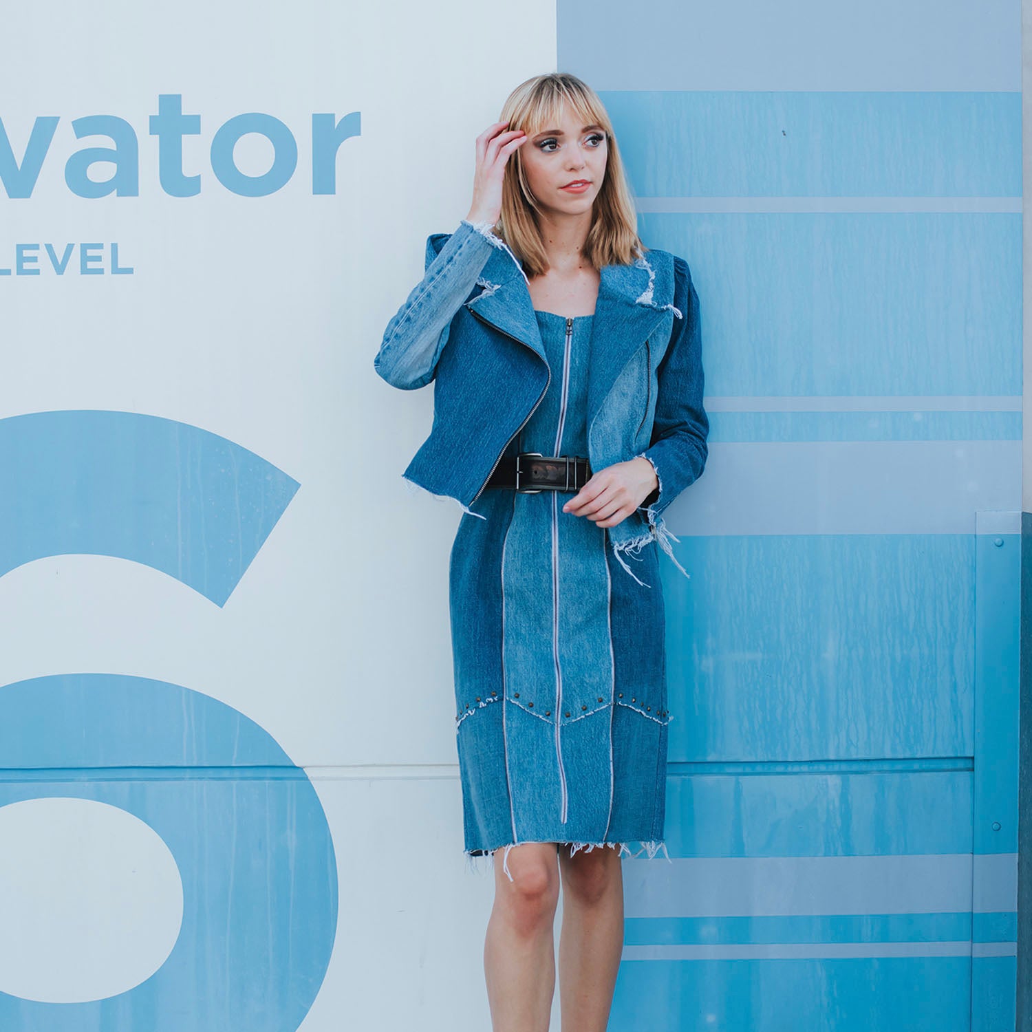 Two-toned fitted denim sheath dress with front zipper, raw edges, princess seam zippers, and metal studs at hem, made from upcycled cotton denim.