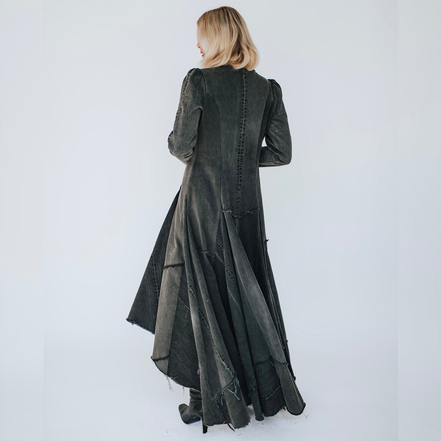 model back view of the Beatrix Coat in distressed black upcycled denim featuring a high-low hem, raw edges, V-neckline, and exposed double zipper closure.