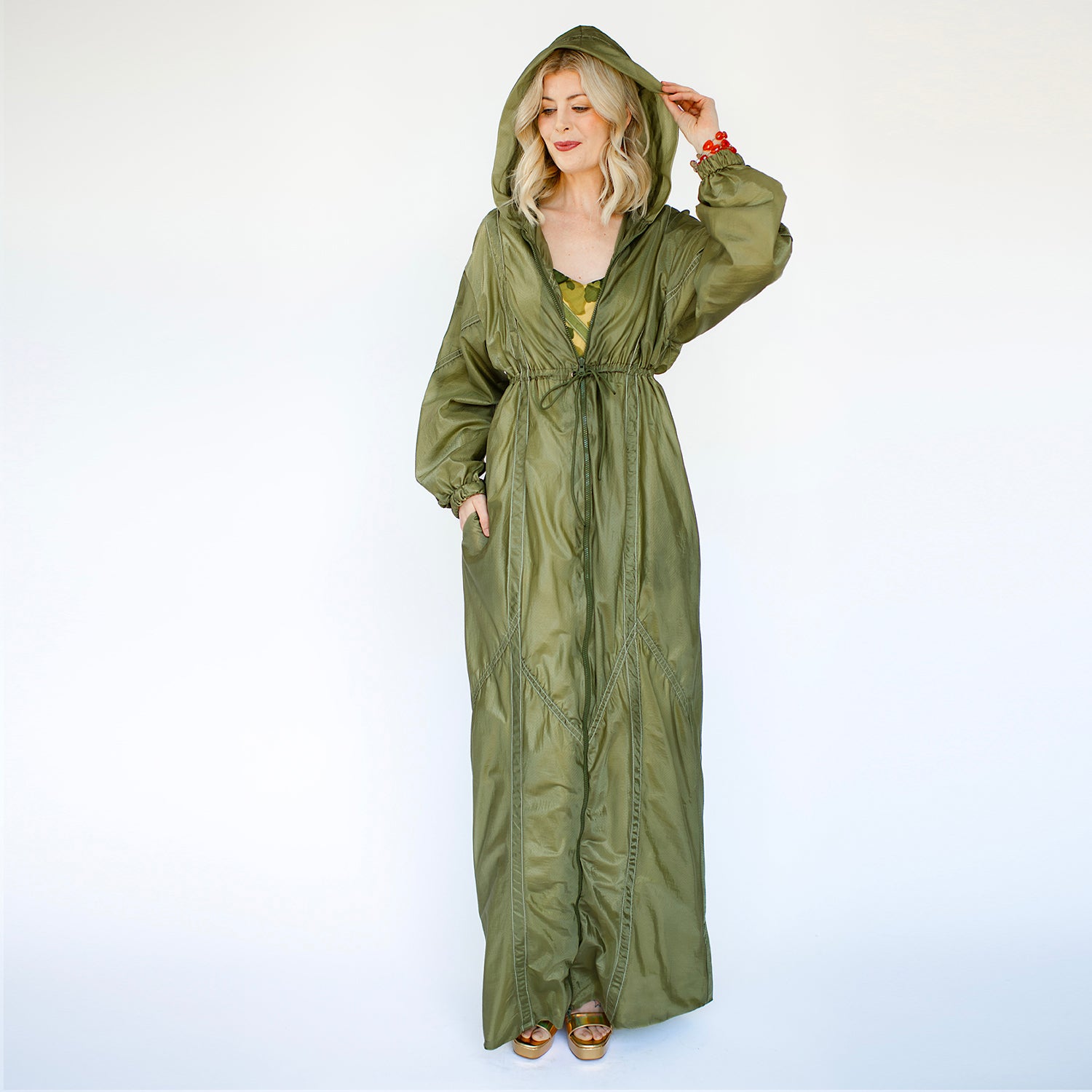 model Olive green full-length bomber coat with hood, drawstring waist, and side pockets, made from upcycled parachute nylon.