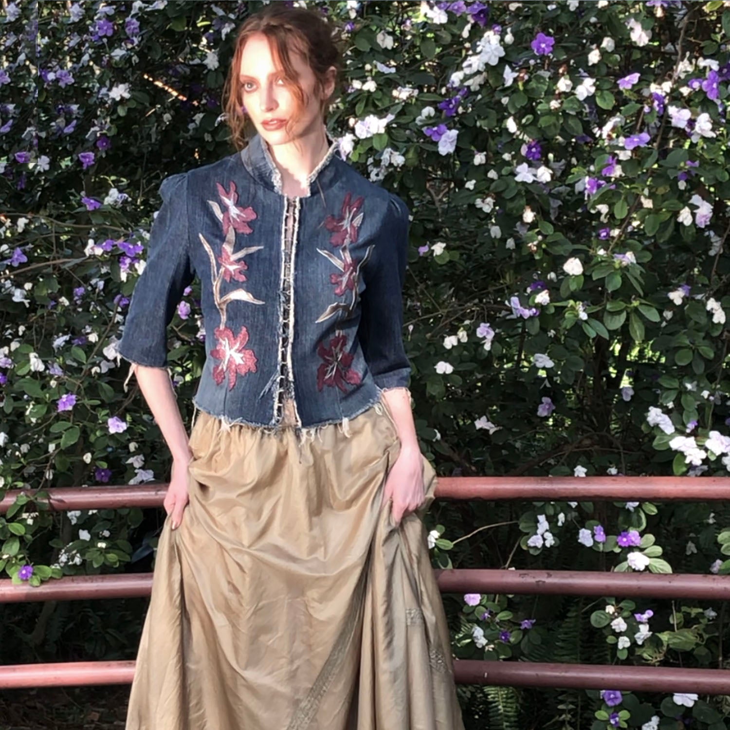 Model in Iris Jacket – upcycled denim jacket with vintage leather floral appliqué, raw hem, and hook closure, shown with gathered elbow-length sleeves.