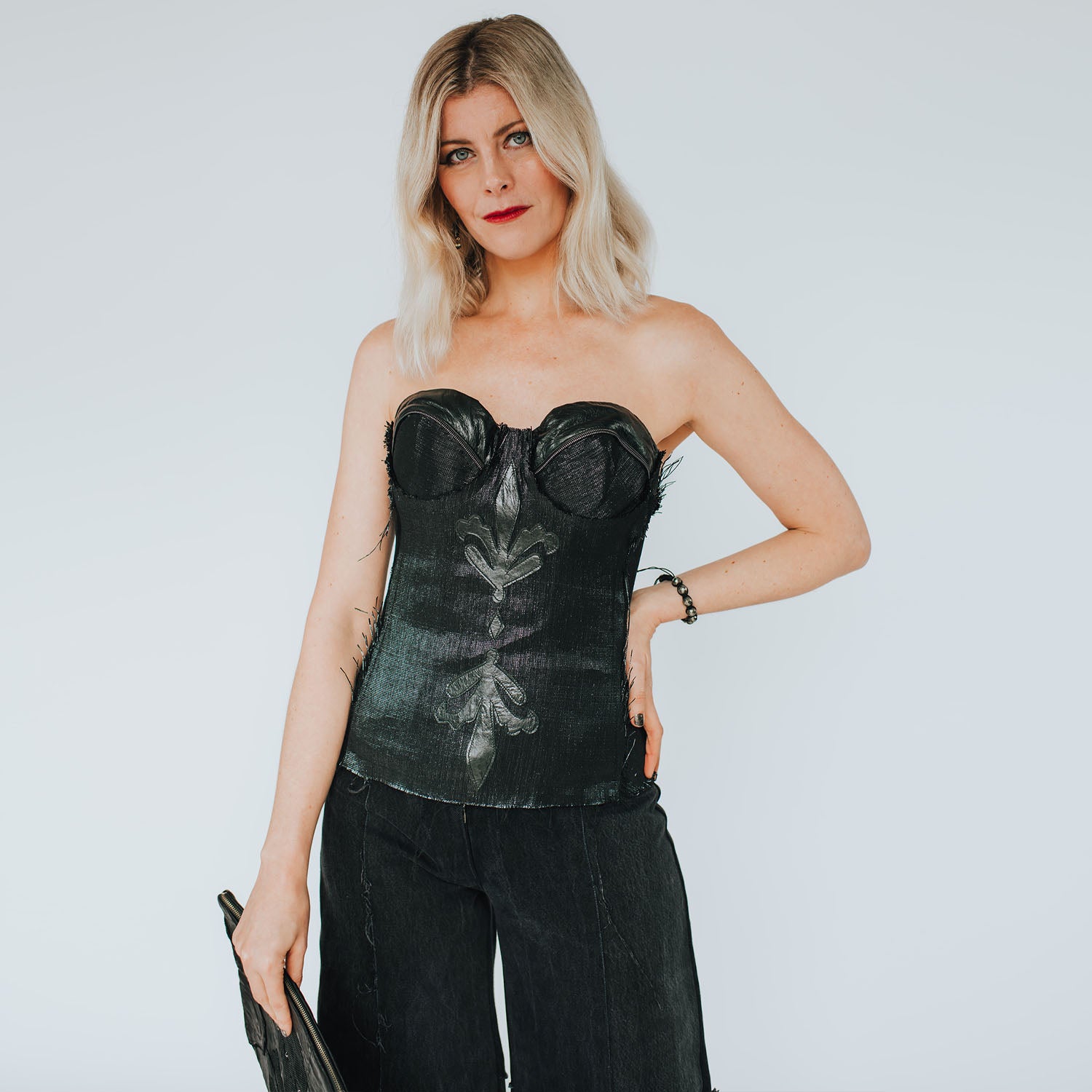 model in Black strapless bustier made from recycled cassette tape fabric, featuring leather appliqués, a front zipper, and eco-conscious steampunk styling.