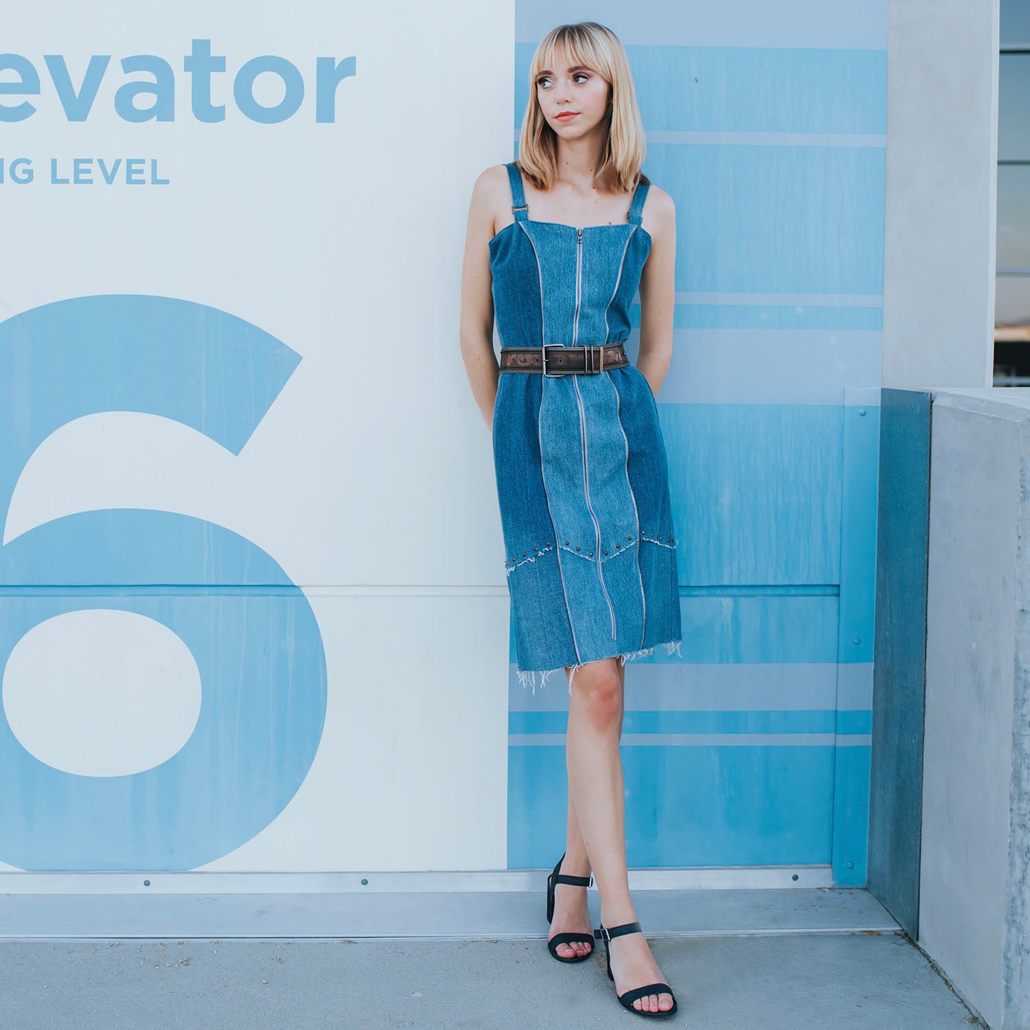 Two-toned fitted denim sheath dress with front zipper, raw edges, princess seam zippers, and metal studs at hem, made from upcycled cotton denim.