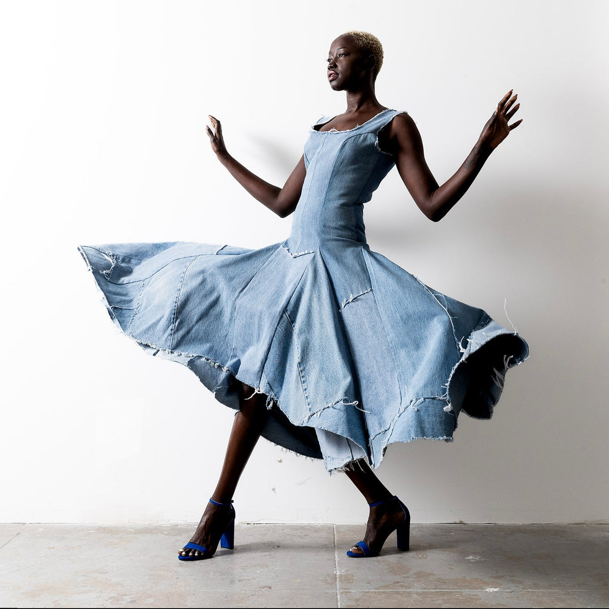 Valerie Dress in bleached denim – Valerie Dress in bleached denim – model twirling in high-low hem dress with dramatic movement and raw-edged finish.
