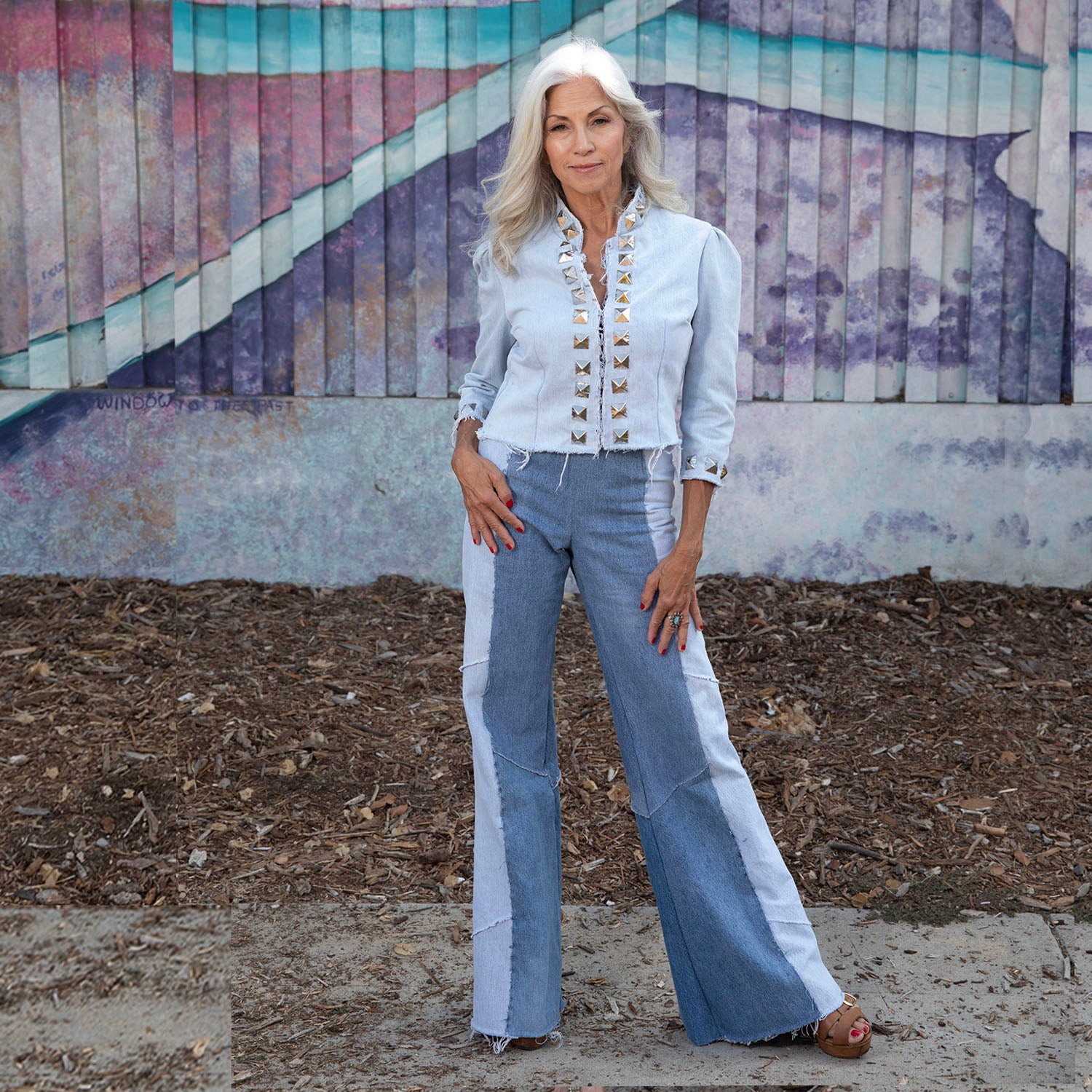 Woman wearing two-tone flared Alice Jeans and matching cropped denim jacket standing outdoors in front of painted mural.
