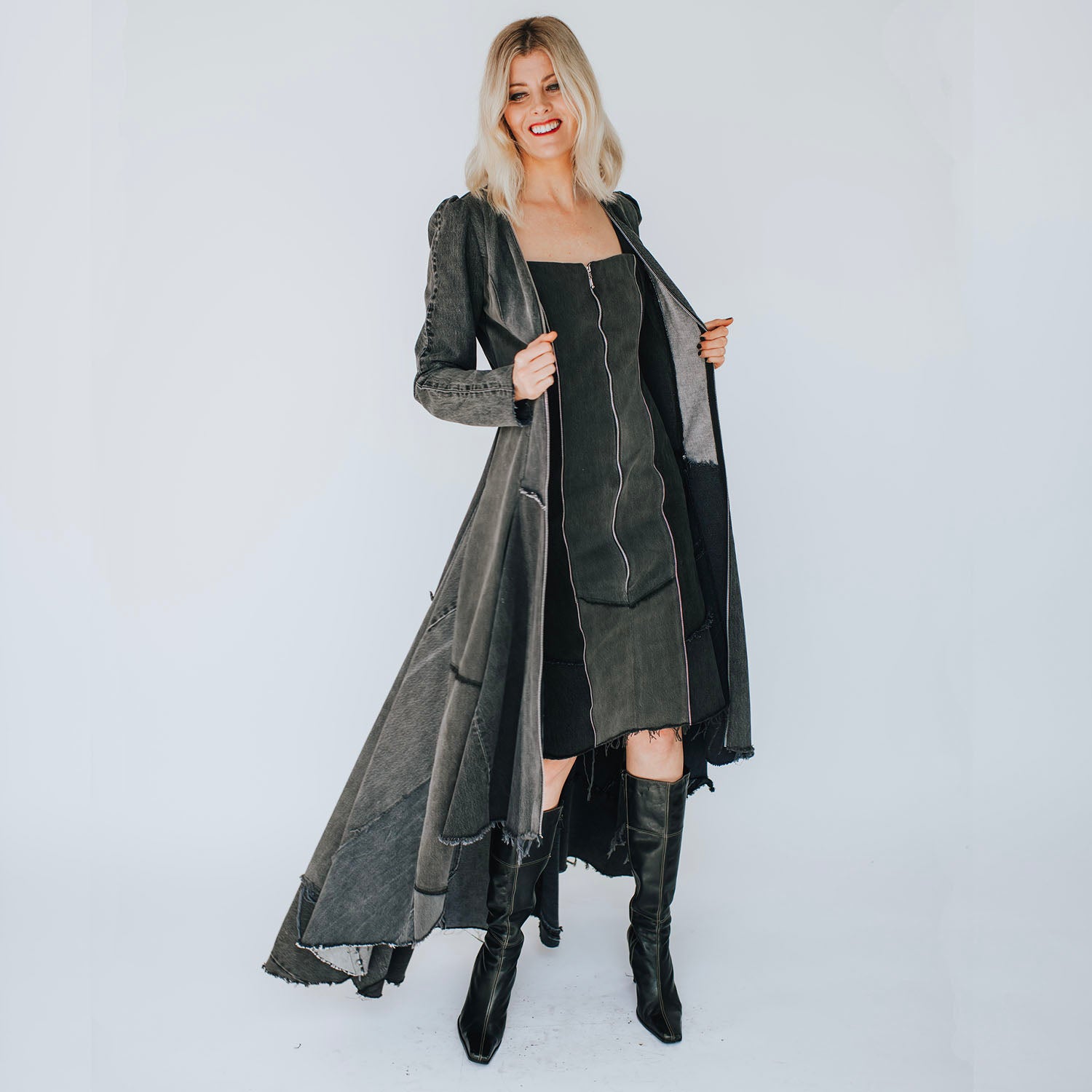 model Front view of the Beatrix Coat in distressed black upcycled denim featuring a high-low hem, raw edges, V-neckline, and exposed double zipper closure.