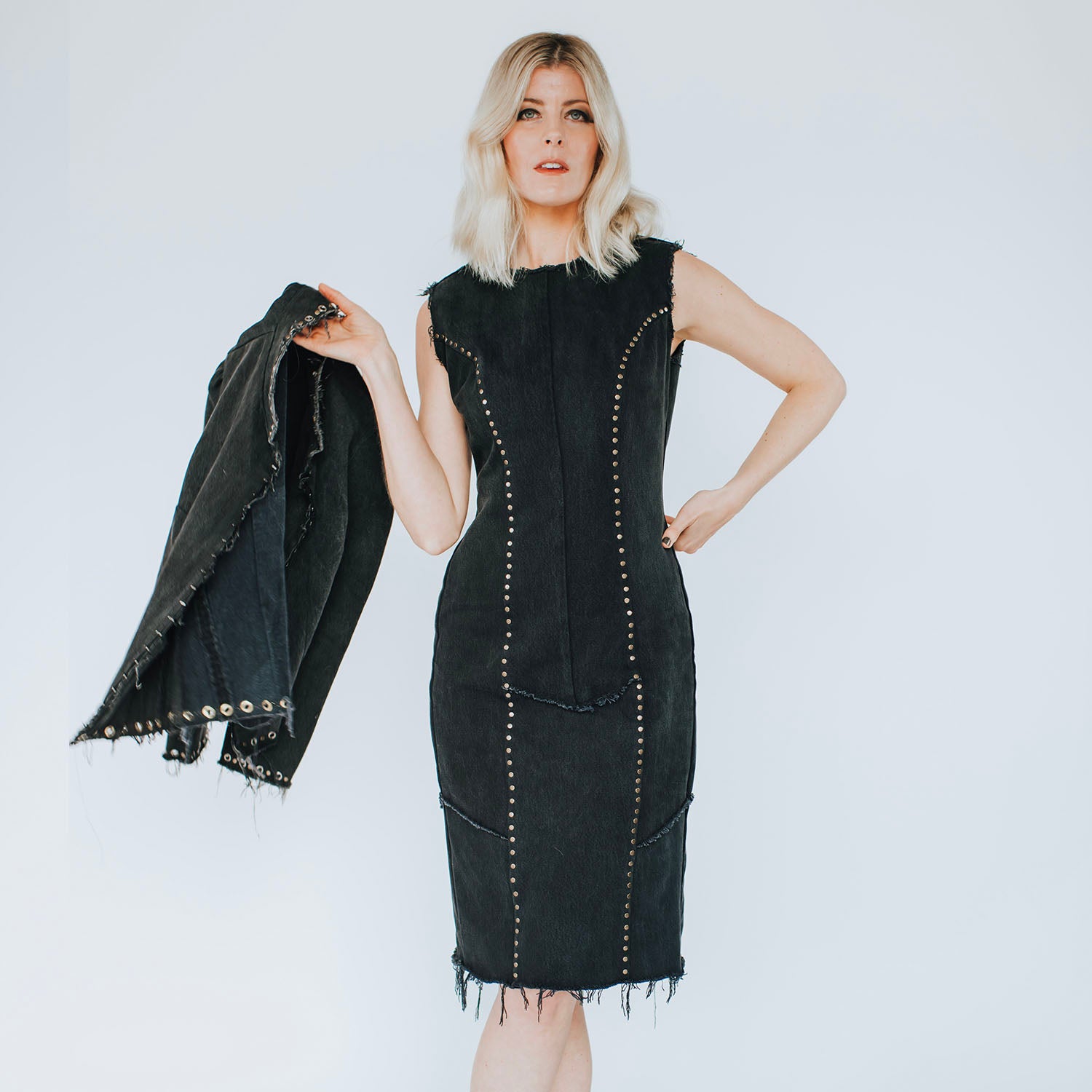 model in  Blair Dress – fitted studded black denim dress with raw-edge hem, antique brass studs, and exposed metal zipper, worn with matching Galena Jacket.