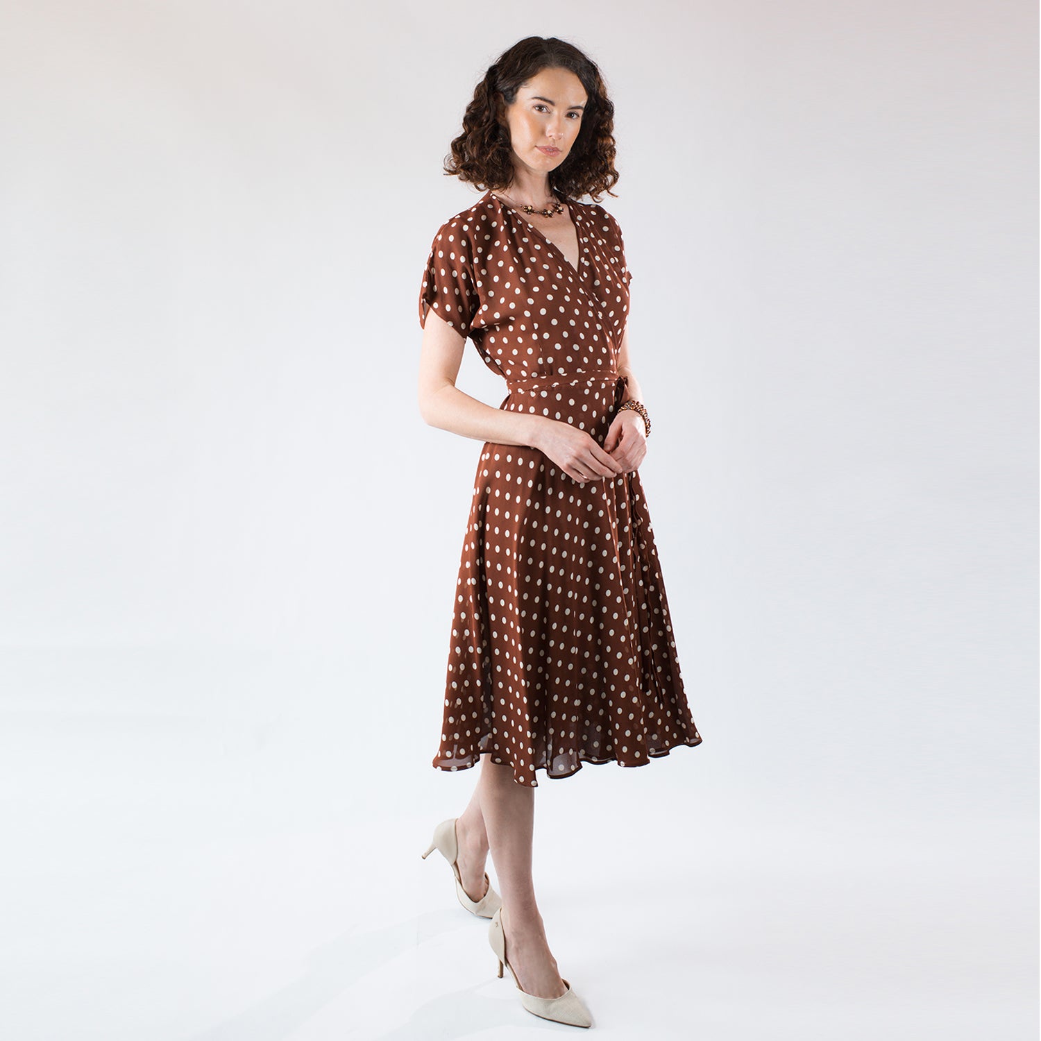 Model wearing the Julia Wrap Dress, a brown and cream polka dot wrap dress made from fluid deadstock rayon crepe with flutter sleeves and a flowing feminine silhouette.