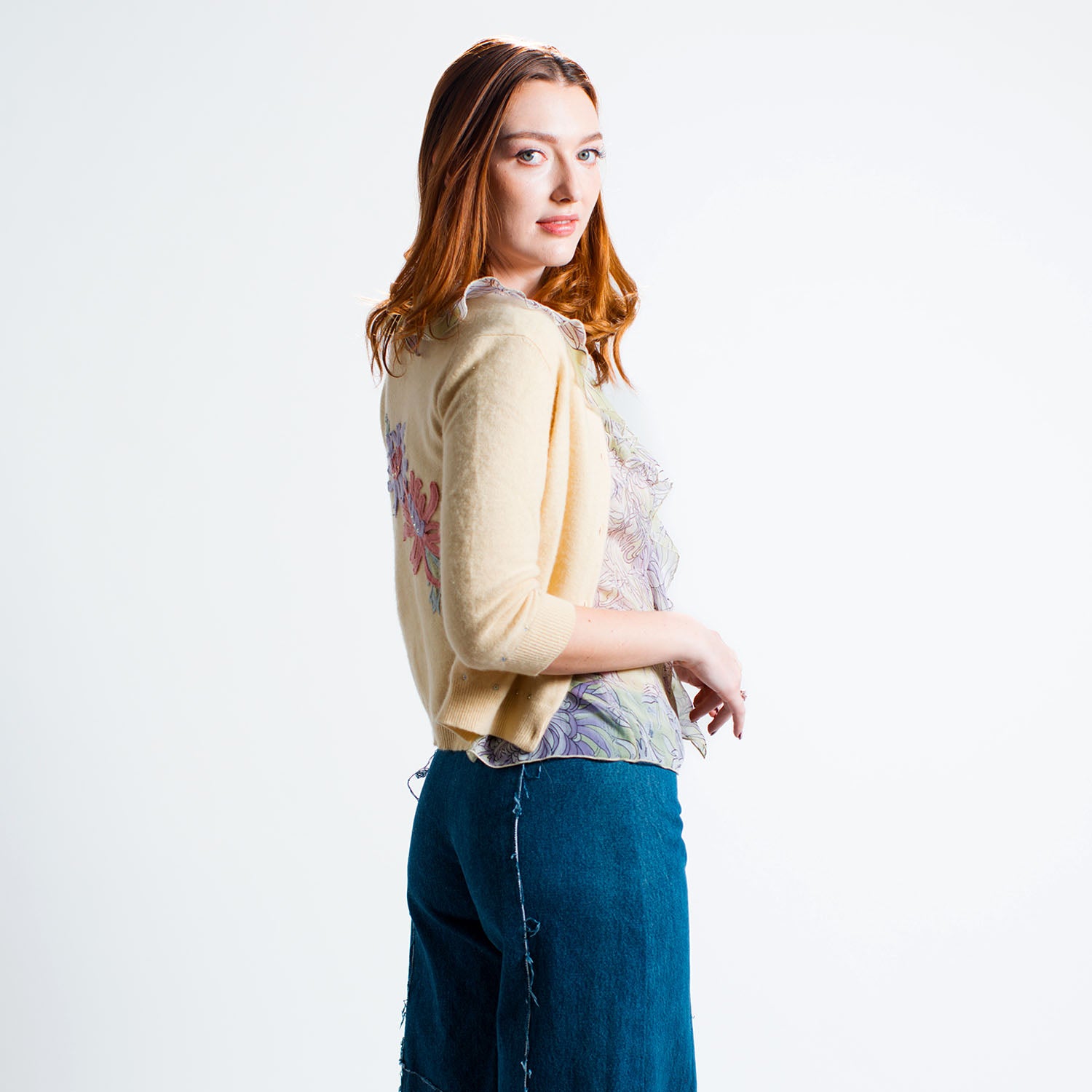 Model wearing the Chrysanthemum Cardigan in cropped yellow cashmere, embellished with floral appliqués and rhinestones, styled over the flounce blouse and wide leg jeans.