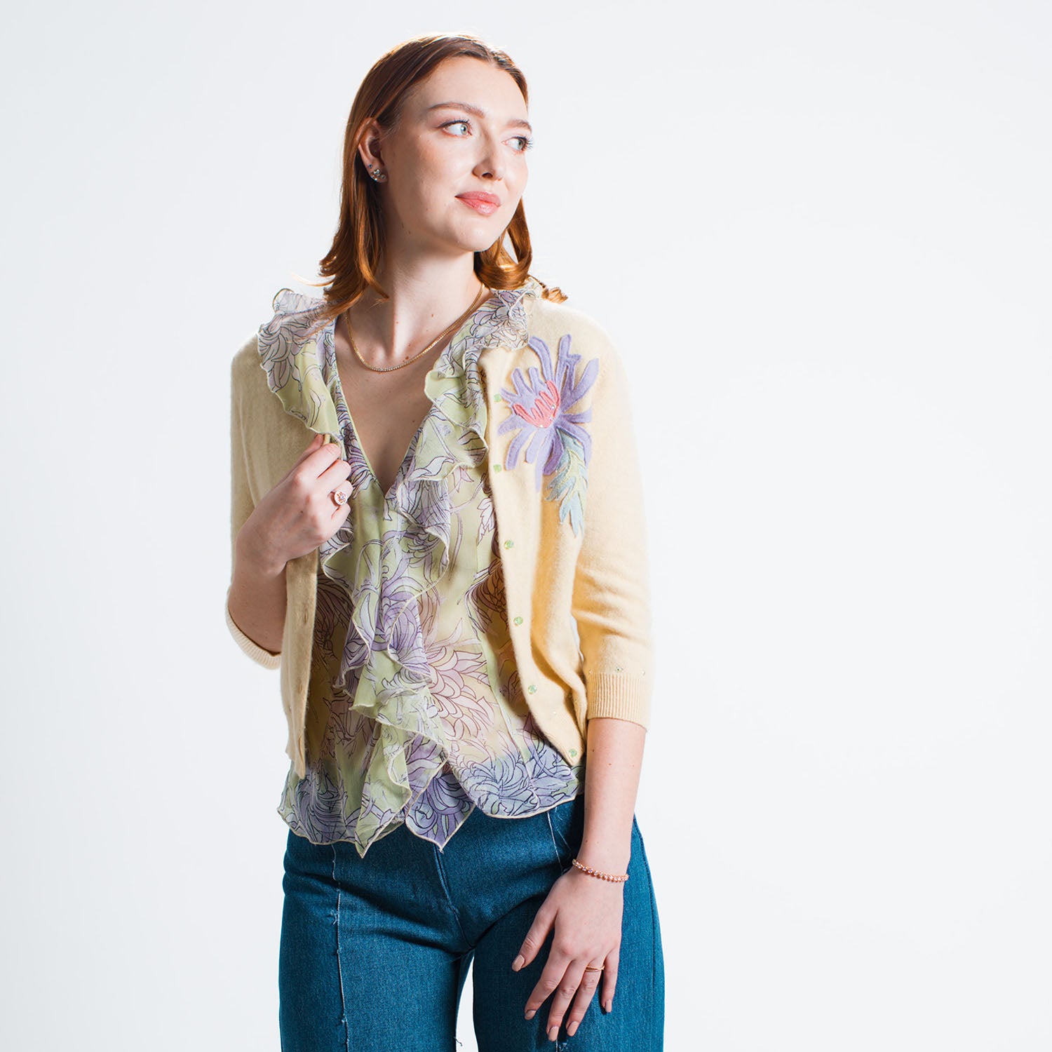 Model wearing the Chrysanthemum Cardigan in cropped yellow cashmere, embellished with floral appliqués and rhinestones, styled over the flounce blouse and wide leg jeans.