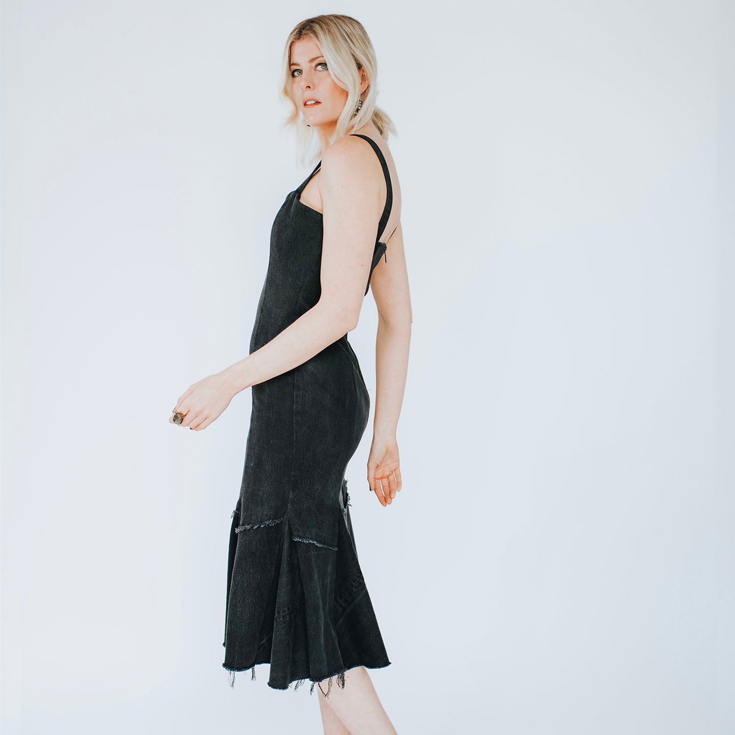 model in Twyla Dress – fit-and-flare upcycled denim dress with raw hem and exposed back zipper, mermaid silhouette shown in black.