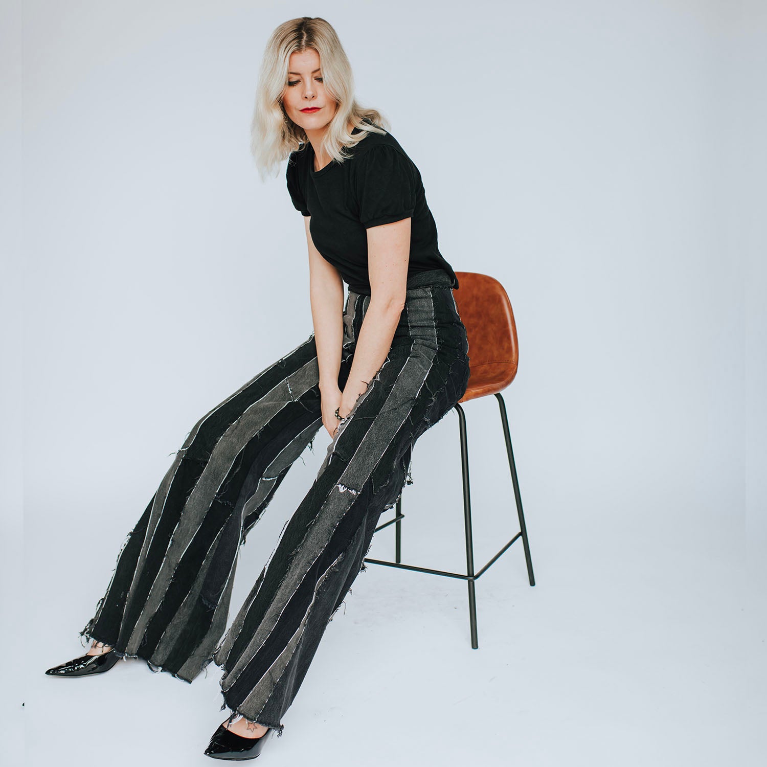model in Wide Leg Layla Stripe Jean – high-waisted wide-leg flare jeans in black upcycled denim with raw-edge vertical panel stripes.