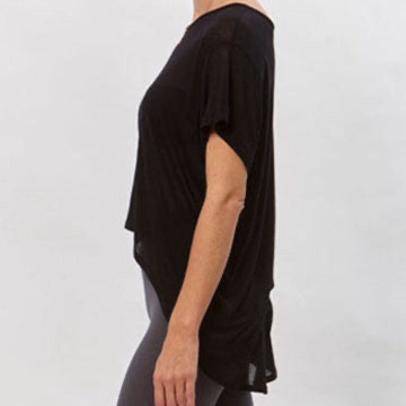 Model wearing the black Alina T-Shirt, a short-sleeved modal top with a high-low hem, paired with dark leggings.