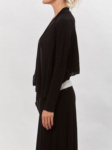Model wearing the Jenna Flutter Front Wrap in black over a white tank and black skirt. Lightweight, draped open-front cardigan.